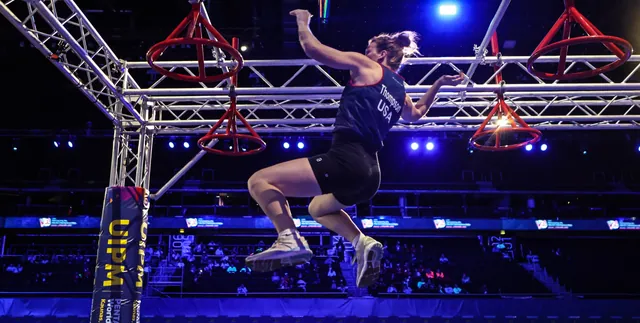 Corinne Thompson in a Team USA top flying between hanging red rings on an arena obstacle course