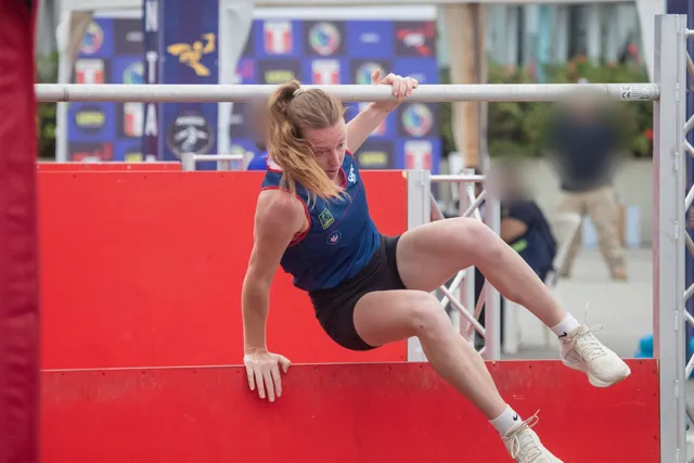 Corinne Thompson swinging her legs over a red wall while holding the bar above it