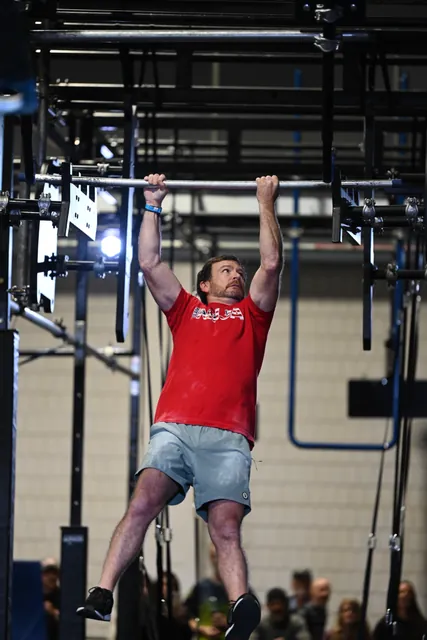 David Kiser in a red Team Ninja shirt swinging from a bar above the crowd