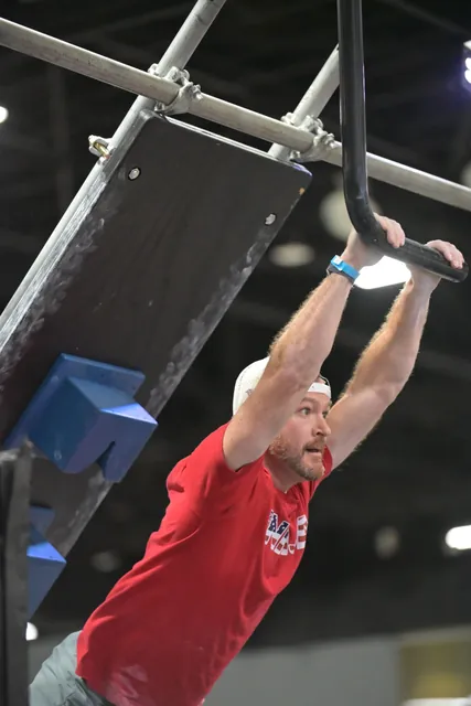 David Kiser in a red Team Ninja shirt reaching for a curved pipe grip