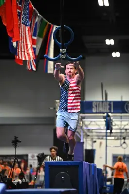 David Kiser in a stars-and-stripes tank leaping from a platform toward a hanging ring