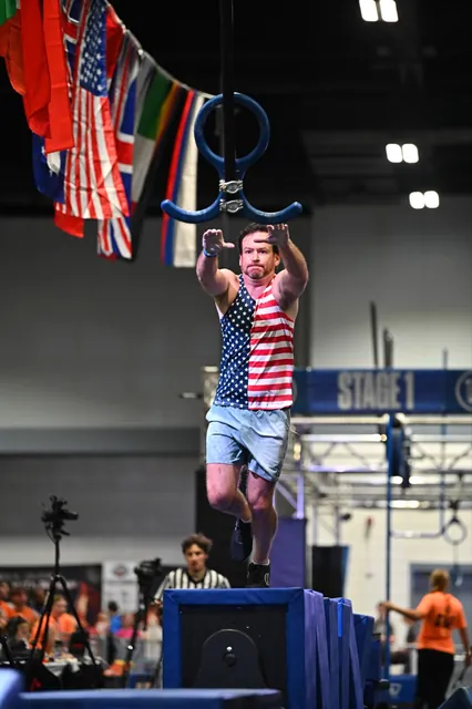 David Kiser in a stars-and-stripes tank leaping from a platform toward a hanging ring