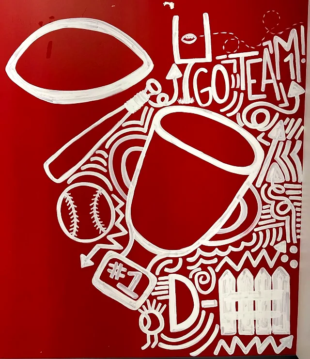 A white hand-painted mural on a red wall in the red party room: a football, goal posts, a bat and baseball, a trophy and the words GO TEAM!