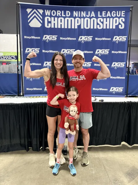 Ashley and David Kiser with their daughter Elliot, flexing in front of the World Ninja League Championships banner