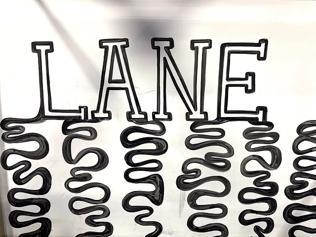 The word LANE hand-lettered in black on a white wall, with wavy black lines dripping down from each letter