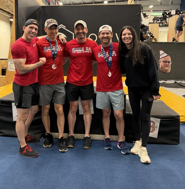 Four NinjaFit Masters athletes in red Team Ninja shirts, two wearing medals, with Ashley Kiser at Motive