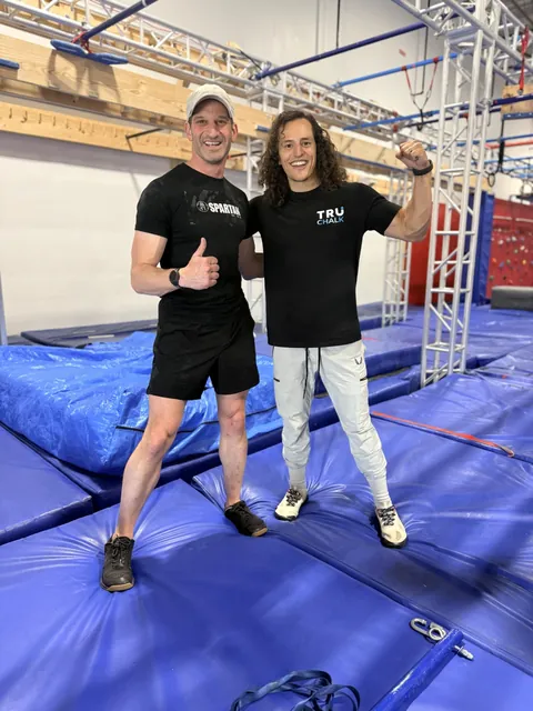 Nicholas Parker giving a thumbs up next to Daniel Gil flexing on the NinjaFit course