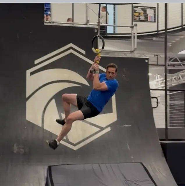 Nicholas Parker swinging from a ring handle in front of a warped wall at Motive