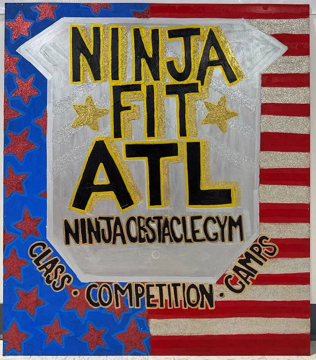 A hand-painted red, white and blue sign at the gym that reads NINJA FIT ATL, Ninja obstacle gym: class, competition, camps