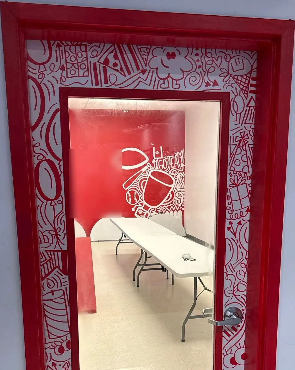 The red party room's door, hand-painted with red doodles, with a red GO TEAM mural and long tables visible through its window