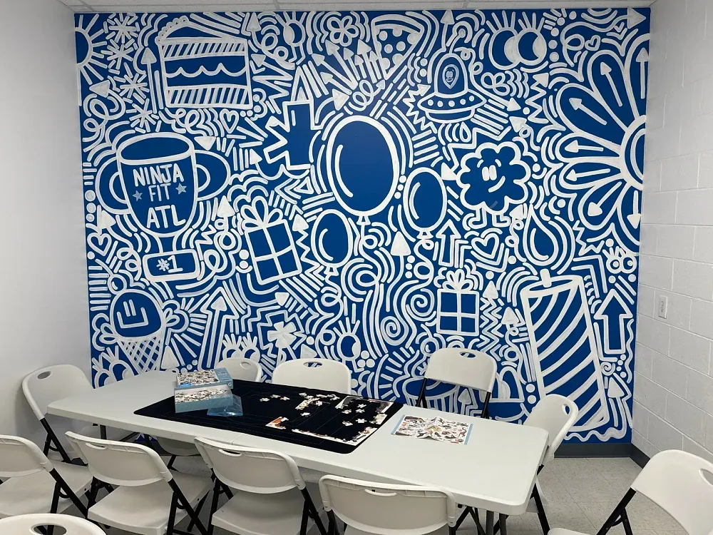 The blue party room: a blue and white hand-painted mural of balloons, presents, cake and a NINJA FIT ATL trophy behind a long table with white chairs