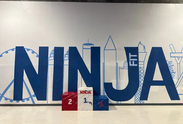 A giant blue NINJA FIT mural with the Atlanta skyline drawn through the letters, and a red, white and blue winners' podium numbered 2, 1 and 3 in front of it