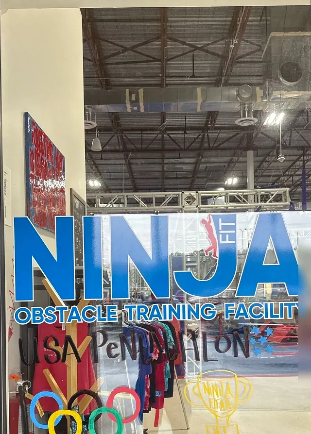 The NINJA FIT logo on the gym window, with NinjaFit shirts on the rack inside