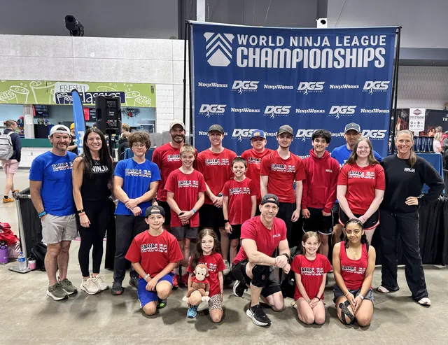 The NinjaFit team in red and blue Team Ninja shirts in front of the World Ninja League Championships banner