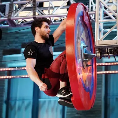 Tyler Gillett gripping a spinning red wheel obstacle