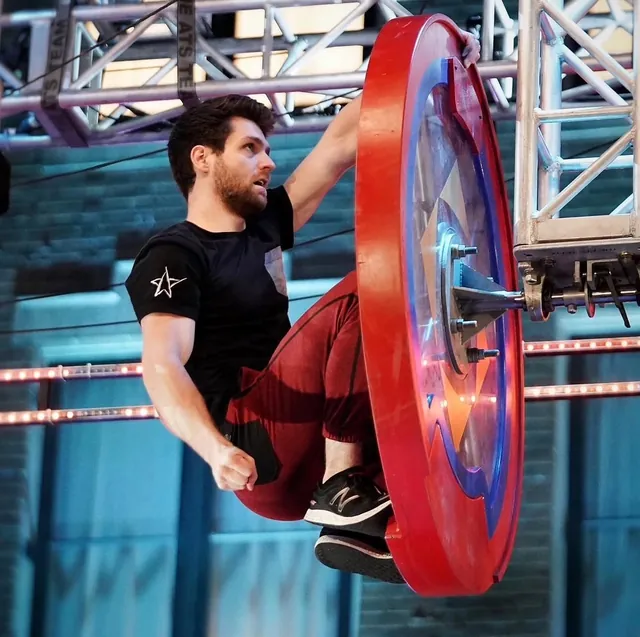 Tyler Gillett gripping a spinning red wheel obstacle