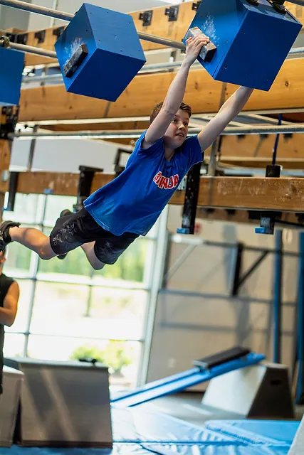 Coach Jackson McGee swinging between hanging blocks on the NinjaFit course
