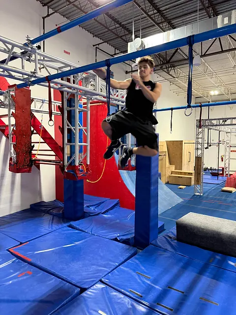 Coach Aiden Burley swinging between rings above the mats