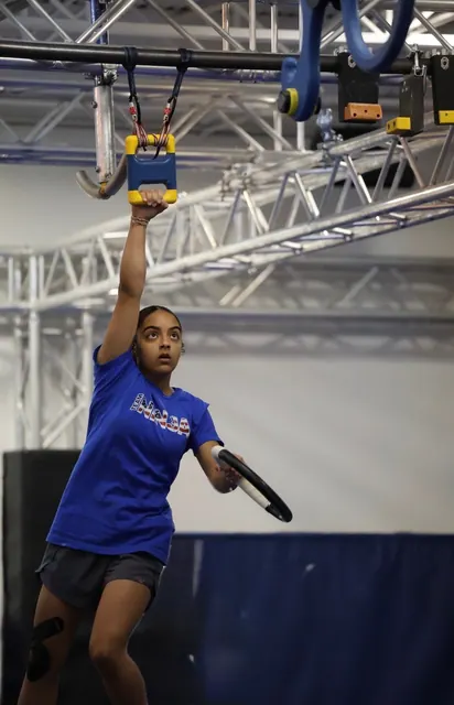 Coach Destiny Cabassa reaching for a hanging grip on the NinjaFit course, holding a ring in her other hand